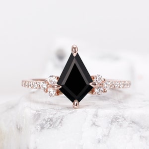 May include: A rose gold engagement ring featuring a black diamond centre stone and a diamond halo. The ring is displayed on a white marble surface.
