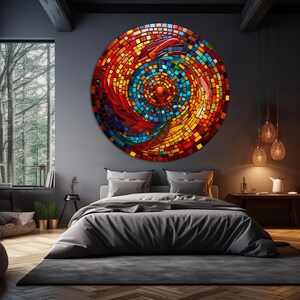 May include: A large circular wall art piece with a mosaic design. The mosaic is made up of small squares of glass in shades of red, orange, yellow, blue, and green. The center of the mosaic is a swirling pattern of red and orange glass. The mosaic is mounted on a dark gray wall in a bedroom setting.