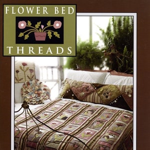 May include: A bed with a floral quilt and decorative pillows. The quilt features a repeating pattern of flowers and stripes in shades of pink, green, and brown. The pillows have embroidered details. The image includes the text "FLOWER BED THREADS".