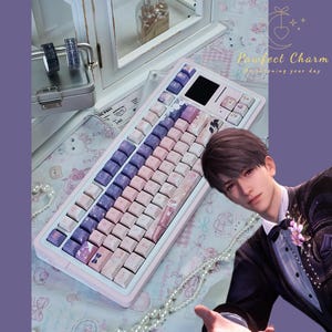 May include: A mechanical keyboard with a white frame and a gradient colour scheme of purple, pink, and white keycaps. The keyboard features a small display screen in the top right corner and custom illustrated keycaps. A digital character is visible.