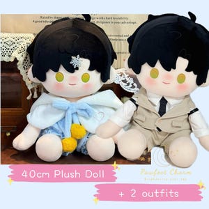Op de afbeelding: Twee 40 cm grote pluche poppen, een draagt een blauwe en witte outfit met een gele pompon en de andere draagt een bruine en witte outfit met een zwarte stropdas. De tekst "Pawfect Charm" en "+ 2 outfits" is zichtbaar in de afbeelding.