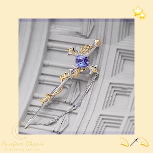 Può includere: Un fermaglio in argento e oro con una pietra preziosa blu al centro. Il fermaglio ha la forma di una spada con una catena attaccata al manico.