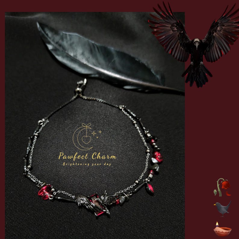 Op de afbeelding: Een zilveren ketting enkelbandje met rode glazen kralen en een bedel van een zwarte vogel met uitgespreide vleugels. Het enkelbandje ligt op een zwart oppervlak met een veer en de tekst "Pawfect Charm Brightening your day".