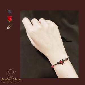 Op de afbeelding: Een zwarte armband van touw met rode hartcharms. De armband zit om een pols.