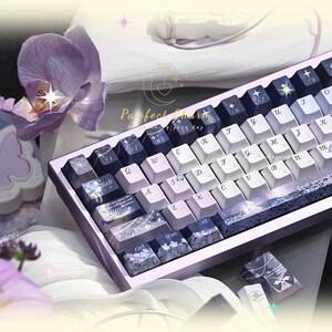 May include: A custom mechanical keyboard with a purple and white color scheme. The keycaps feature a mix of white, lavender, and dark blue keys with various designs. The keyboard has a matching purple frame and the text "Perfect Charm" is visible.