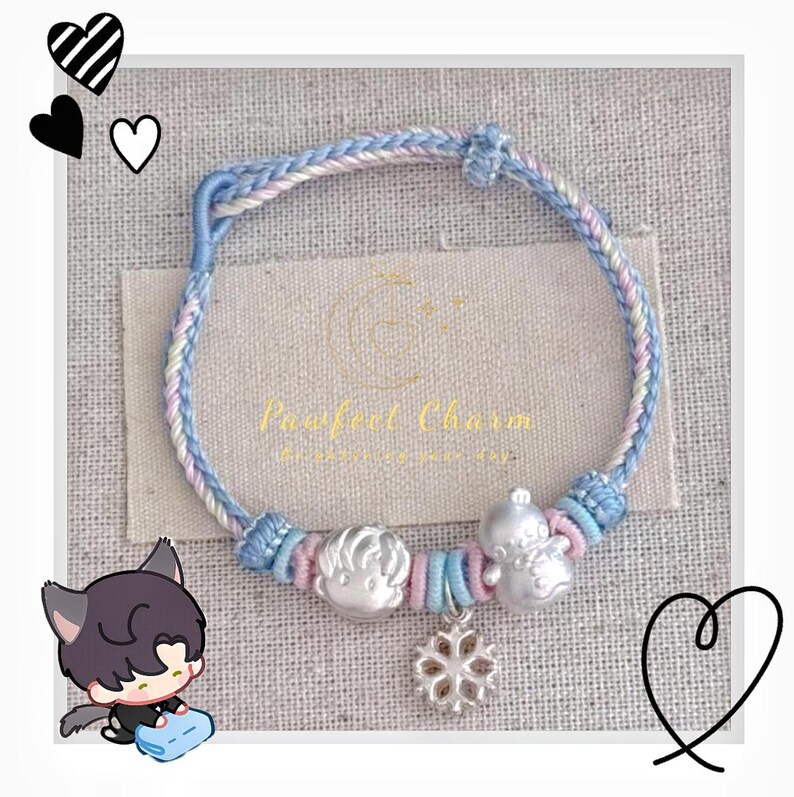May include: A braided bracelet with blue, pink, and white threads. The bracelet features silver charms of a boy, a snowman, and a snowflake. The text "Pawfeel Charm" is visible on the background.