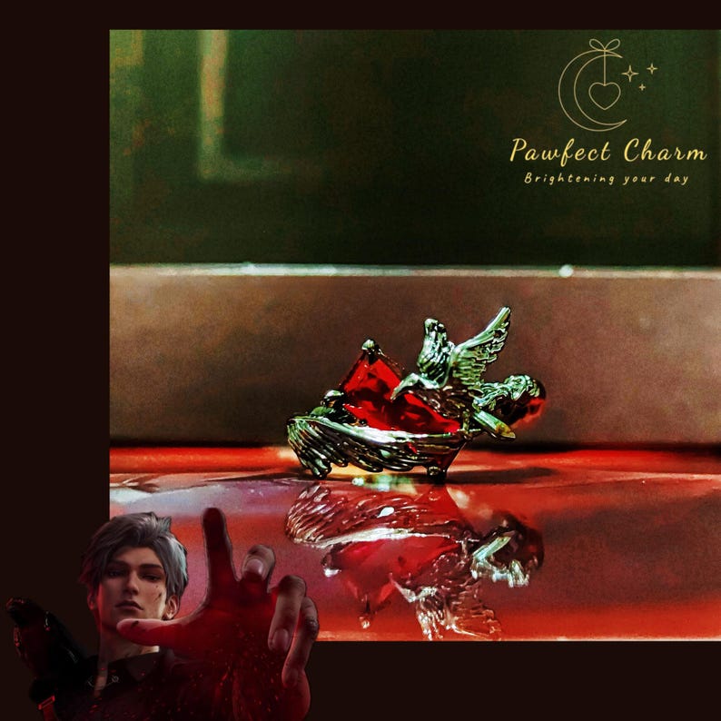 May include: A silver charm with a red heart and angel wings. The charm is on a red surface and reflects in the surface. The text "Pawfect Charm Brightening your day" is in the top right corner of the image.