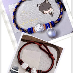 May include: Two braided bracelets. One is blue, brown, and black with a silver apple charm and a round charm. The other is red and black with a silver owl charm, feather charm, and round charm. Both are on a white background.