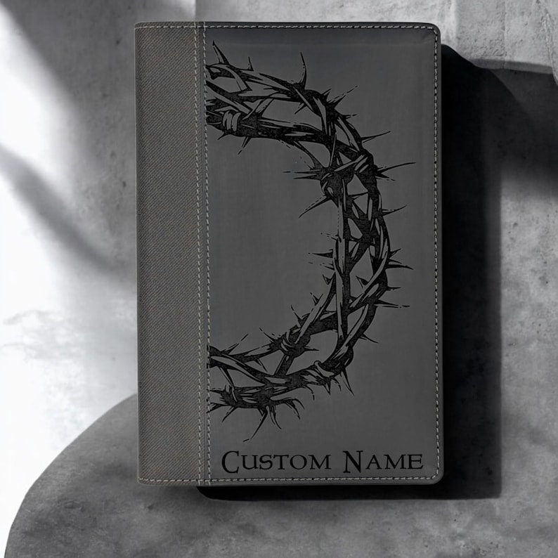 Op de afbeelding: Grijs lederen dagboek met een zwart doornenkroonontwerp en de tekst "CUSTOM NAME" op de voorkant.