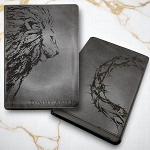 May include: Two gray leather journals with different designs. One features a lion's head and the name "TOMMY ARD JR" engraved on the front. The other features a crown of thorns design.
