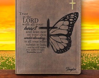 Könnte beinhalten: Ein braunes, lederartiges Notizbuch mit einem Schmetterlingsflügel-Design und einem Kreuz. Der Text lautet: "Vertraue auf den HERRN von ganzem Herzen... Sprüche 3:5-6." Das Notizbuch hat einen genähten Rand und den Namen "Taylor".