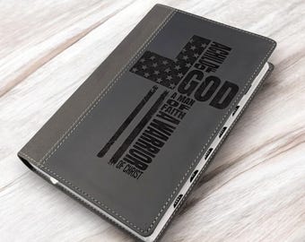 Op de afbeelding: Grijs lederen notitieboek met een zwart kruisontwerp en de woorden "A Man of Faith, God, American Warrior, Son of Christ" gedrukt op de omslag.