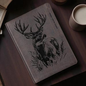 May include: Gray leather journal with a detailed black engraved image of a buck deer with large antlers. The journal has a stitched border and the text "Only Serious About" is printed vertically on the right side.