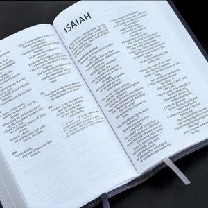 Op de afbeelding: Een open Bijbel met het boek Jesaja en het Hooglied zichtbaar. De pagina's zijn open om de tekst in zwarte letters op wit papier te tonen. De Bijbel is gebonden in een donkergrijze omslag met een zilveren bladwijzer.