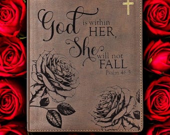 Könnte beinhalten: Ein braunes Lederjournal mit der Aufschrift "God is within HER, She will not FALL" und Psalm 46:5. Das Cover zeigt eingravierte Rosenillustrationen und ein goldenes Kreuz. Umgeben von roten Rosen.