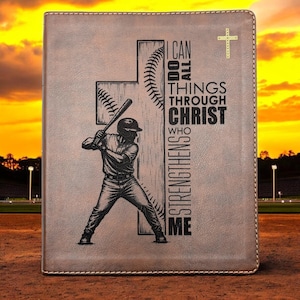 May include: A brown rectangular leather-like book cover featuring an engraved baseball player holding a bat in front of a cross shaped like a baseball. The text reads I CAN DO ALL THINGS THROUGH CHRIST WHO STRENGTHENS ME with a small cross icon.