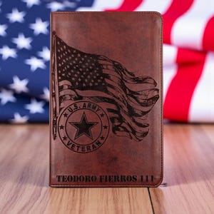 Könnte beinhalten: Eine braune Ledergeldbörse mit einer detaillierten Gravur der amerikanischen Flagge und dem Schriftzug "U.S. ARMY VETERAN" in einem sternförmigen Emblem. Der Name "TEODORO FIERROS 111" ist unten eingraviert. Die Geldbörse ist rechteckig.