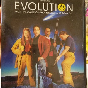 May include: DVD case for the movie "Evolution" featuring David Duchovny, Orlando Jones, Seann William Scott, and Julianne Moore. The cover art shows the cast in a science fiction setting with the title and a smiley face.