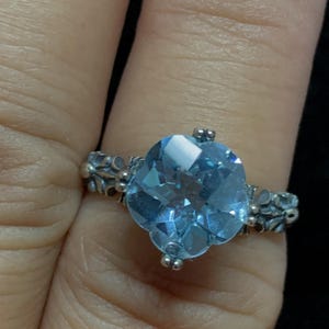 May include: A silver ring with a large, light blue gemstone set in a floral design.