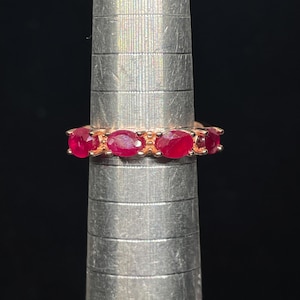 May include: A rose gold band ring with a row of oval-shaped ruby gemstones.
