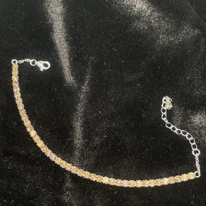 May include: A silver bracelet with a row of small, round, light brown stones. The bracelet has a lobster clasp closure.