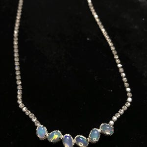 May include: A silver necklace with a row of five oval-shaped opals and a chain of small, clear rhinestones.