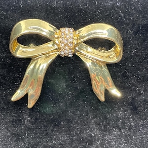 May include: A gold-toned bow brooch with clear rhinestones in the center.