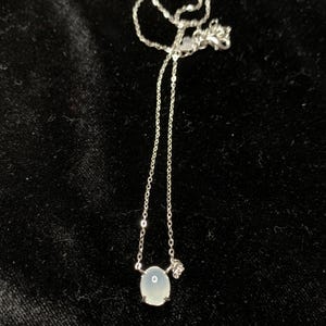 May include: A silver chain necklace with a light blue oval pendant.