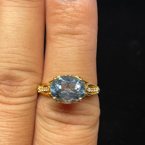 May include: A gold ring with a large oval blue gemstone surrounded by smaller clear gemstones.