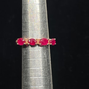 May include: A gold band ring with six red ruby stones set in a prong setting.
