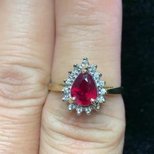 May include: A pear-shaped ruby ring set in yellow gold with a halo of smaller diamonds.
