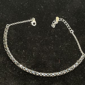 May include: A silver bracelet with a row of black stones. The bracelet has a lobster clasp closure.