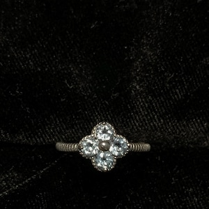 May include: A silver ring with a four-leaf clover design set with clear stones.