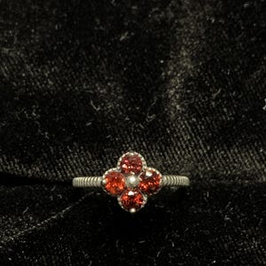 May include: A silver ring with a red gemstone flower design.