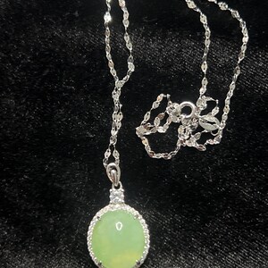 May include: A silver chain necklace with a round green jade pendant set in a silver bezel with small clear stones around the edge.