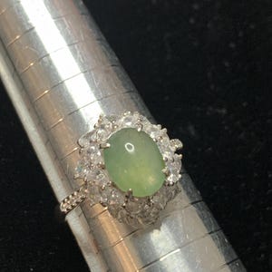 May include: A silver ring with a green oval gemstone surrounded by clear round stones.