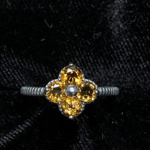 May include: A silver ring with a flower design featuring five yellow gemstones.