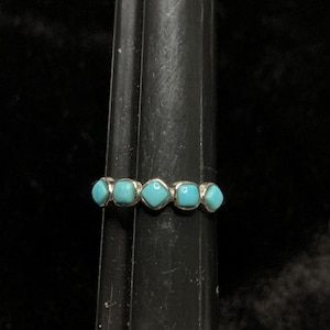 May include: A silver ring with five turquoise stones set in a row. The stones are square shaped and have a light blue color.