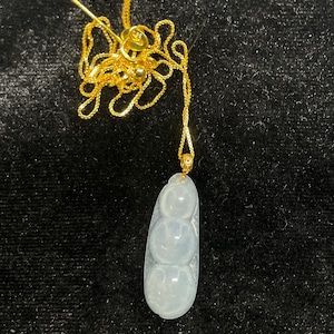 May include: A white jade pendant with a gold chain. The pendant is shaped like three round beads.