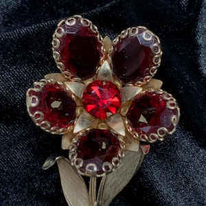 May include: A red rhinestone flower brooch with gold-toned metal accents. The flower has five petals and a center stone.