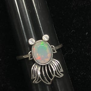 May include: A silver ring with a white opal gemstone and two smaller clear gemstones. The ring features a delicate floral design.