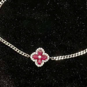 May include: A silver chain bracelet with a red ruby and diamond flower charm.