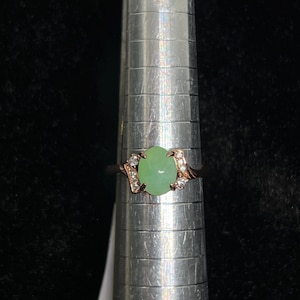 May include: A green jade ring with a rose gold setting and small diamonds around the stone.