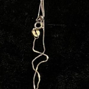 May include: A silver necklace with a delicate chain and a light green, octagonal pendant. The pendant has an etched design. The necklace is displayed against a dark background.