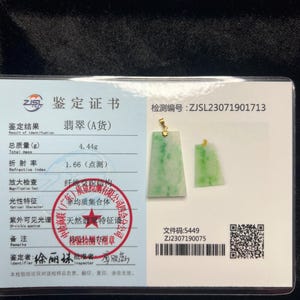 May include: Two jade pendants with gold accents rest on a certificate. The pendants are rectangular with a light green hue. The certificate displays Chinese text, a red stamp, and a QR code. The total mass of the jade is 4.44g.