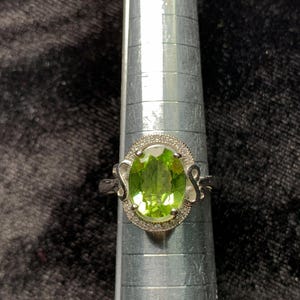 May include: A silver ring with a large oval green gemstone surrounded by smaller clear gemstones.