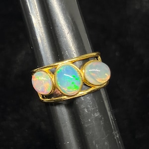 May include: A gold ring with three oval-shaped opals set in a band. The opals are white with a hint of green and pink.