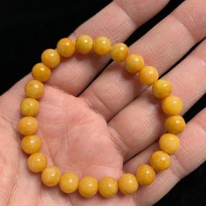 May include: A yellow beaded bracelet with a smooth, polished finish. The beads are round and uniform in size, creating a classic and elegant look.