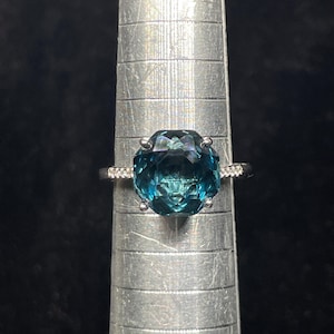 May include: A silver ring with a large, faceted, teal blue gemstone. The ring is on a silver ring sizer.