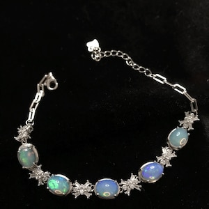 May include: A silver bracelet with five oval-shaped opal stones and small diamond-like accents. The bracelet has a lobster clasp closure.